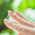 Broken nail on a woman’s hand with a manicure on a green background